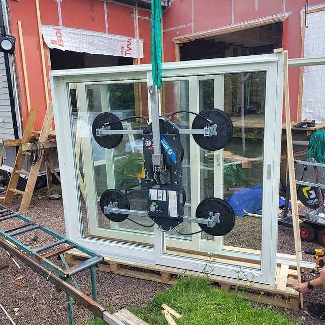 Stor skyvedør i glass løftes med vakuumløfter foran bolig under oppføring.