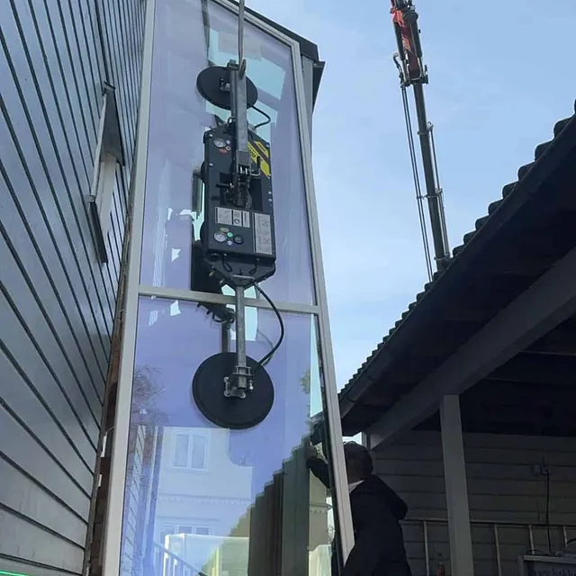 Høy glassrute monteres vertikalt med vakuumløfter ved vegg på bolig.