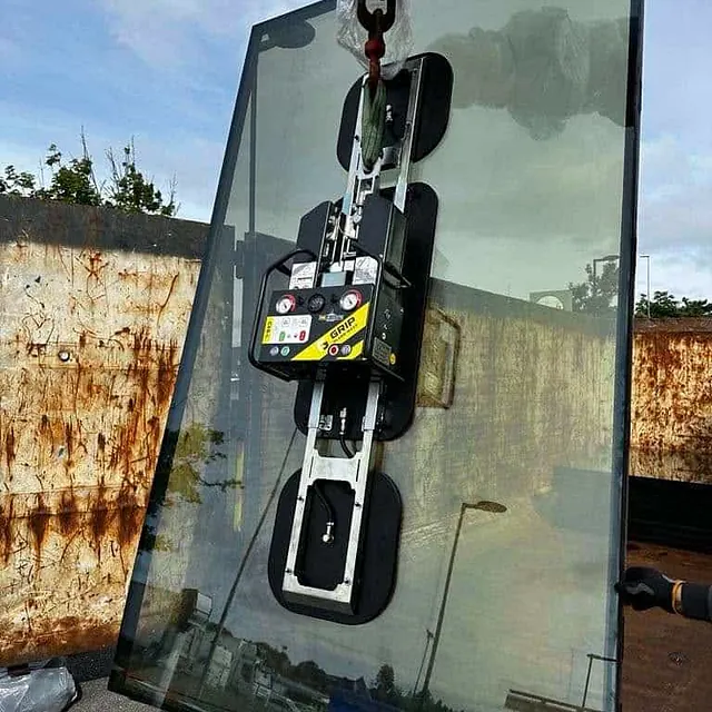 Glassplate håndteres med vakuumløfter foran rusten vegg under transport eller montering.